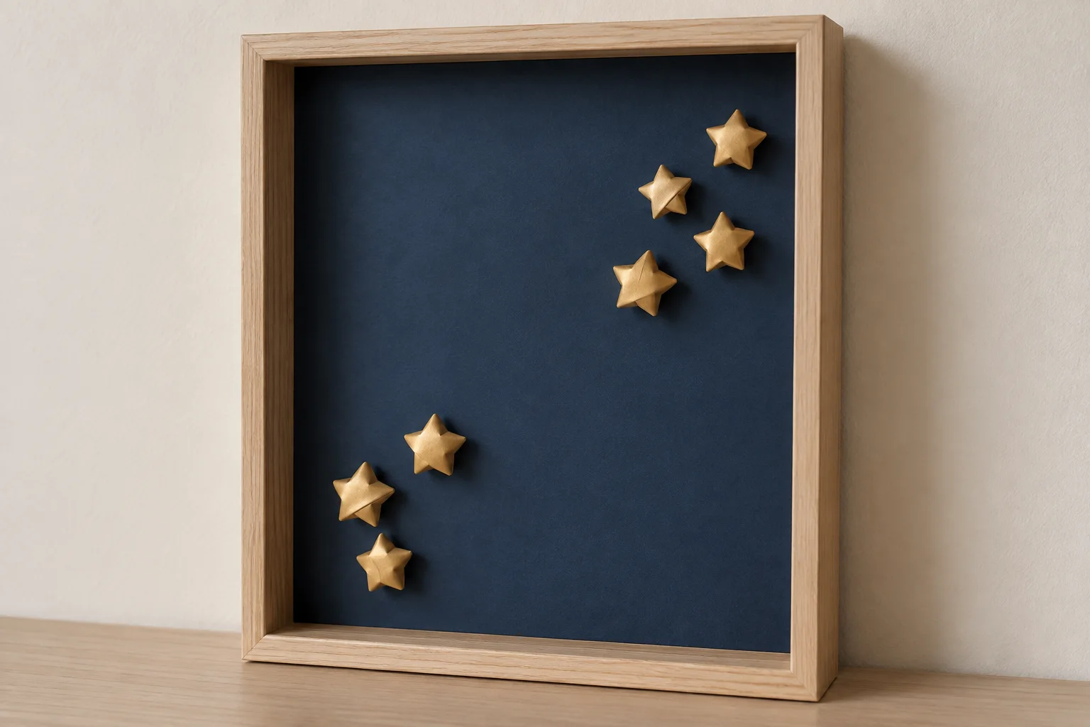 Sept petites étoiles en papier doré dans un cadre profond à fond bleu nuit.